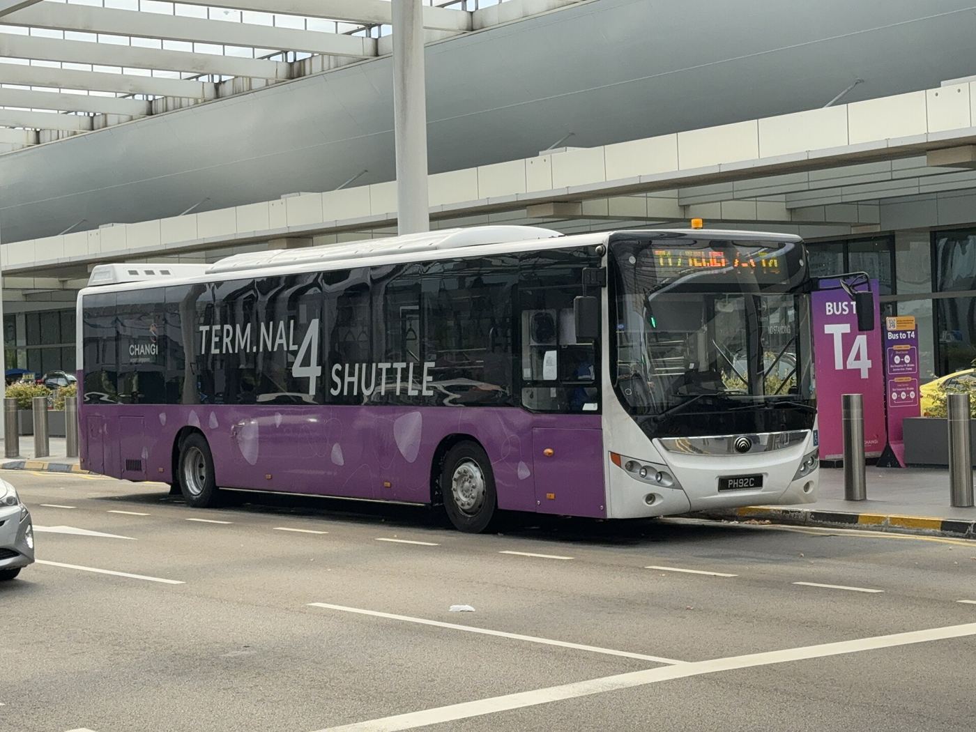 Passengers board an airport shuttle bus outside a busy modern terminal.