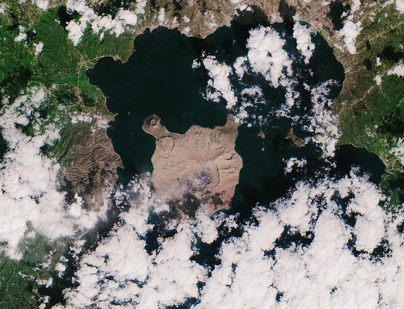 island volcano with ash cloud above dark lava fields reaching the sea