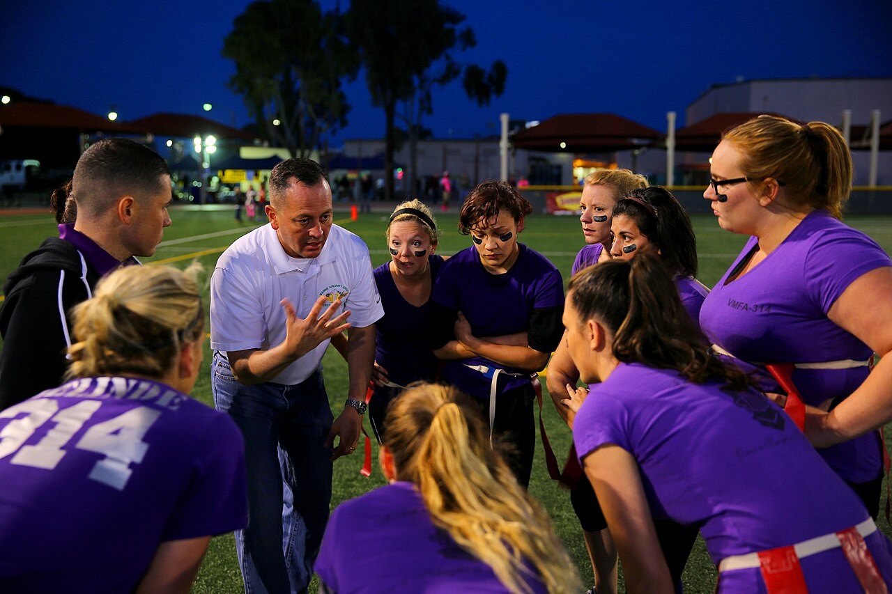 A football team in a huddle with their coach during a night game under lights